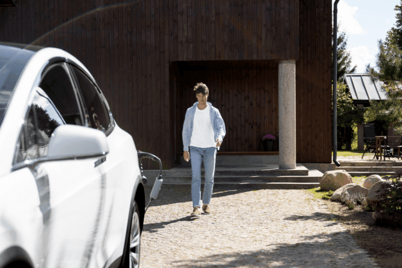 Man wandelt thuis naar zijn elektrische wagen die aan het laden is aan zijn eigen laadpaal op de oprit