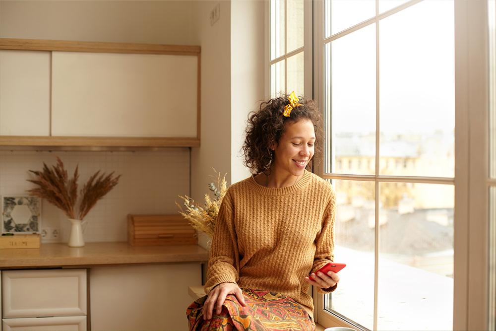 Vrouw geniet van de warmte van de zon aan het raam in haar duurzaam verwarmd huis